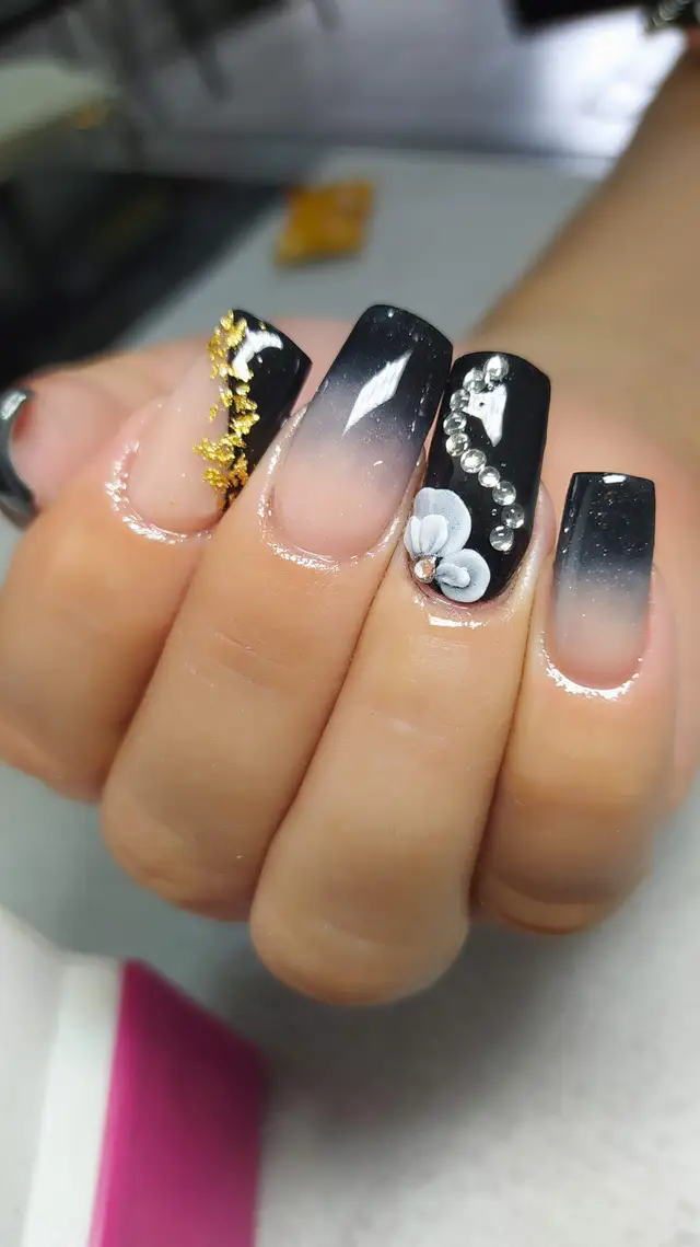 Uñas acrílicas en negro con detalle floral y hoja de oro